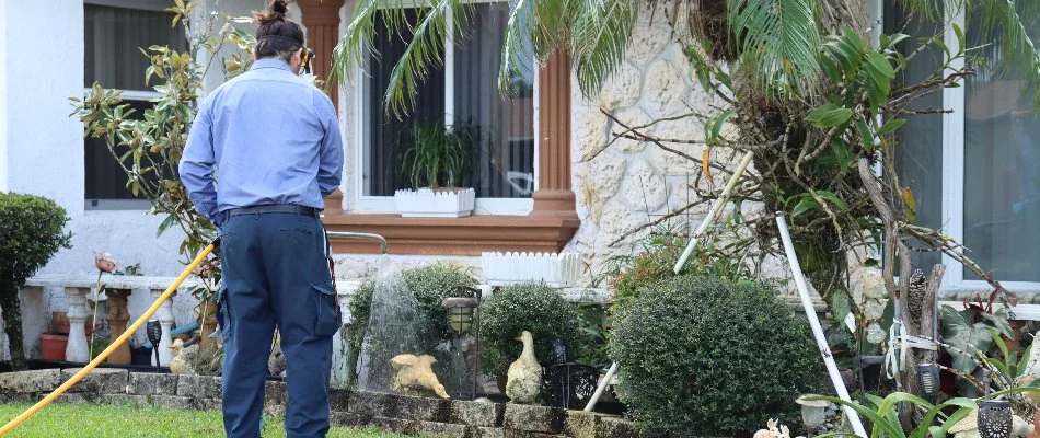 Tech spraying around a house in Miramar, FL, for pests.