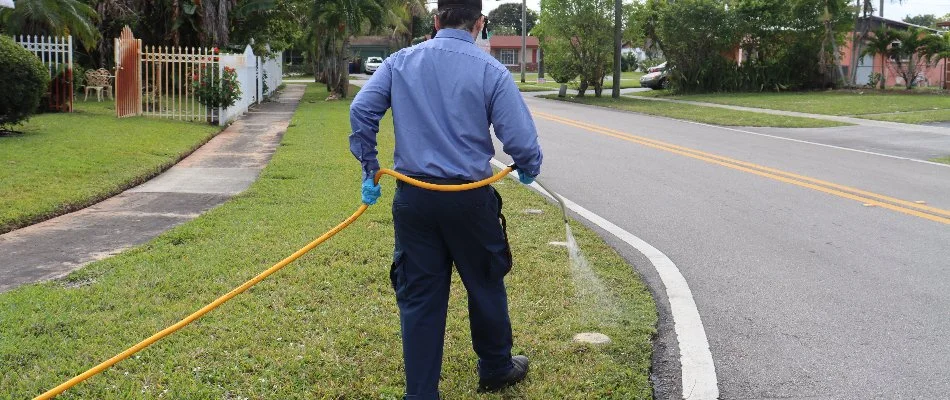 Worker wearing a blue shirt applying a lawn care treatment to a lawn in Dania Beach, FL. 